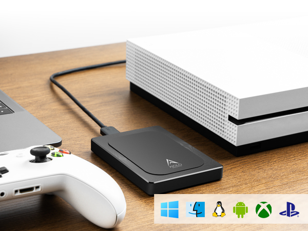 Gaming setup with white console, black external hard drive, and controller on wooden surface. Logos indicate compatibility with multiple operating systems and gaming platforms.