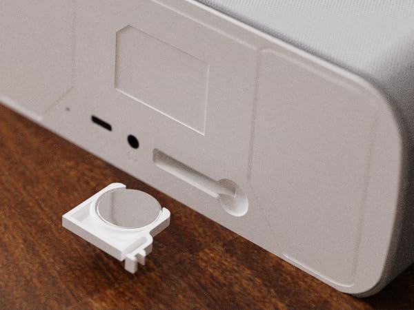 Bedside alarm clock with open compartment on wooden table, scattered jewelry, modern and functional.