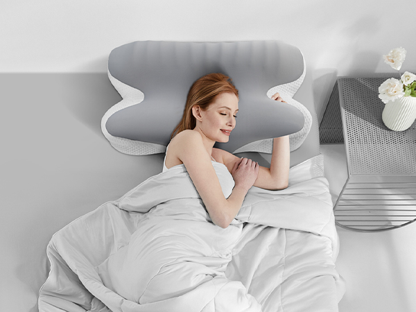 Gray butterfly-shaped pillow on a bed with white bedding. Pillow has curved wing-like extensions and a contoured center for head support.