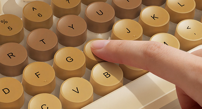 Finger pressing beige round keycaps on wireless keyboard for smooth responsive typing feel