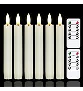 Six white LED taper candles with flame-like tips, illuminated. Two white remote controls with buttons for timer and mode settings are visible beside the candles.
