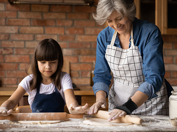 White and navy checkered apron worn by person demonstrating rolling dough on wooden surface. Visible features include adjustable neck strap and waist ties.