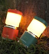 Two portable lanterns, one red and one teal, emitting warm light. Compact design with mesh-covered light panels and handles for carrying.