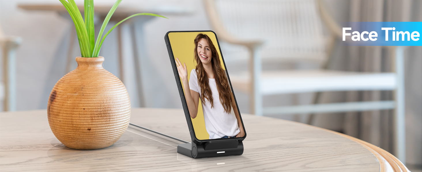 Smartphone on charging stand displaying video call interface. Wooden table with spherical vase and green plant. 'Face Time' text overlay in corner.